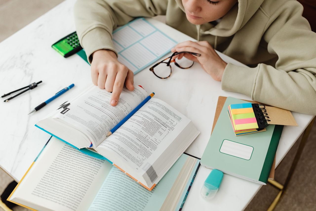 Young student focused on studying with textbooks, calculator, and notes on a desk.