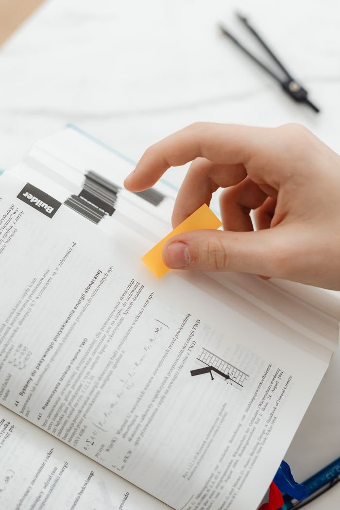 A hand places a sticky note on a book page for marking important information.