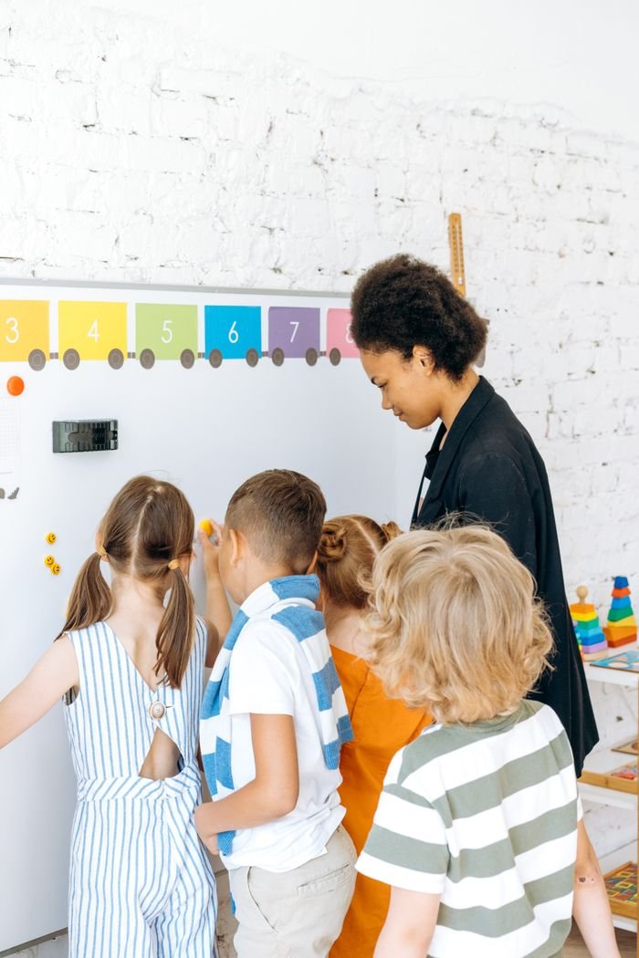 Children engaged in learning with a teacher at a colorful classroom whiteboard.